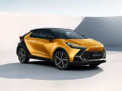 Nowy, złoty Toyota C-HR Hybrid z czarnym dachem prezentuje się dynamicznie na tle minimalistycznej architektury.