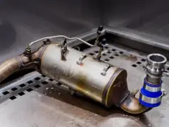 Metalowy element układu wydechowego, prawdopodobnie zawór EGR, leży na metalowej powierzchni.