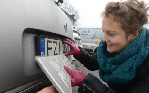 Kobieta w czerwonych rękawiczkach montuje tablicę rejestracyjną. Nowa gs rejestracja czeka na samochód.
