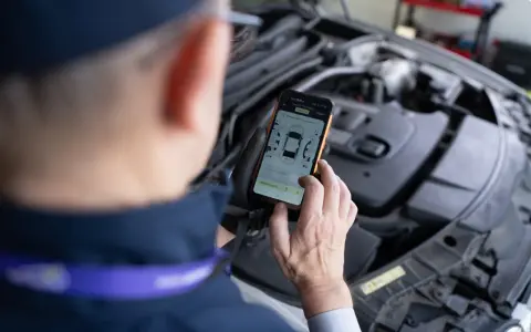 Mechanik sprawdza raport DTC na telefonie, analizując pomiar lakieru i szczelin w samochodzie.