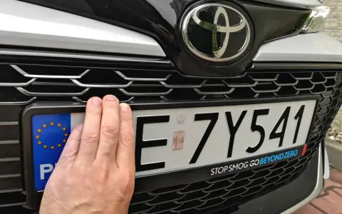Dłoń zasłania część tablicy rejestracyjnej E 7Y541. Pod nią widoczny jest napis "STOP SMOG GO BEYOND ZERO".