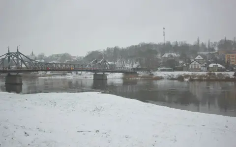 Most na rzece w zimowy dzień, śnieg pada. W tle zabudowania i drzewa. To piękna dx rejestracja krajobrazu.