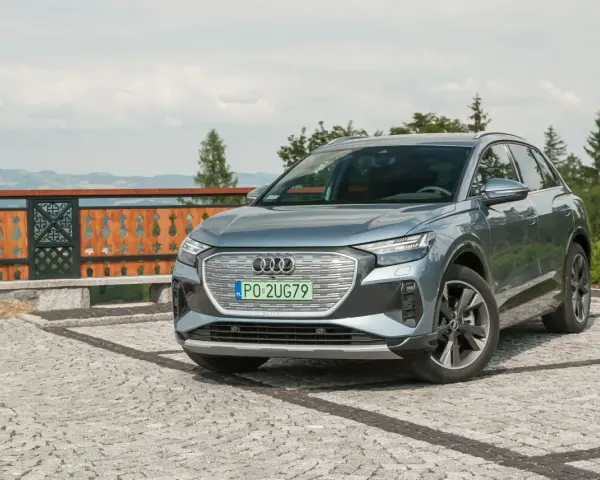 Szary Audi Q4 na kamienistym podjeździe, z widokiem na góry i las.