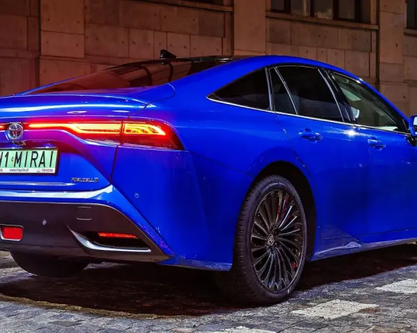 Niebieska Toyota Mirai z podświetlonymi światłami tylnymi stoi na brukowanej ulicy nocą.