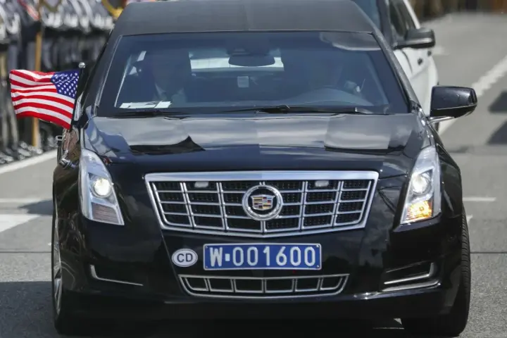 Czarny Cadillac z amerykańską flagą i tablicą rejestracyjną CD W-001600, wskazującą na rejestracje dyplomatyczne.