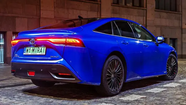 Niebieska Toyota Mirai z podświetlonymi światłami tylnymi stoi na brukowanej ulicy nocą.