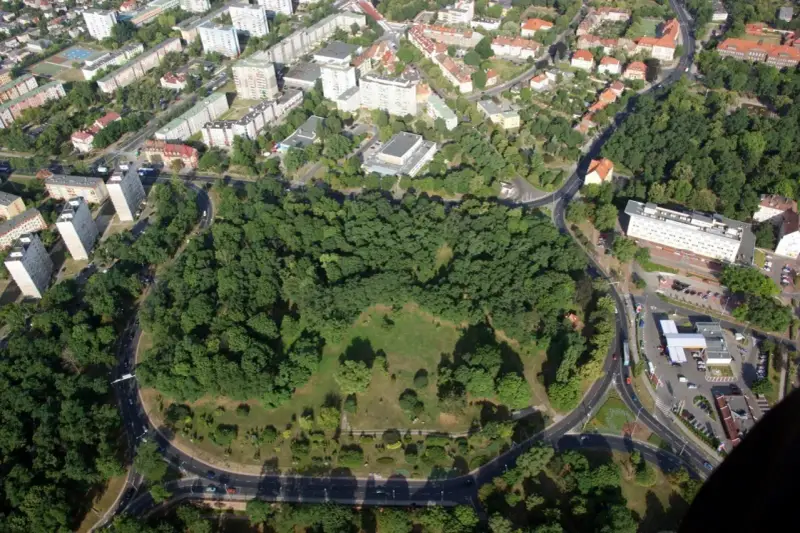 Widok z lotu ptaka na zielony park otoczony drogami, z budynkami mieszkalnymi w tle. To największe rondo w Polsce, które otacza serce miasta.