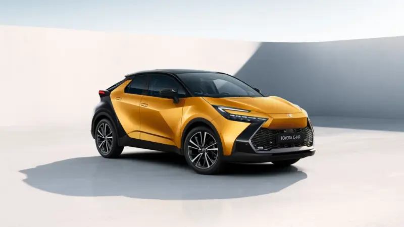Nowy, złoty Toyota C-HR Hybrid z czarnym dachem prezentuje się dynamicznie na tle minimalistycznej architektury.